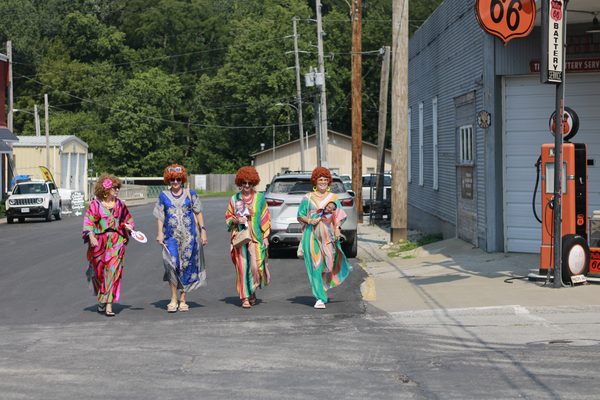 Four Mrs. Roper Romp participants stroll toward Main Street in colorful caftans, red wigs and oversized accessories Saturday, Aug. 8, in Weston.